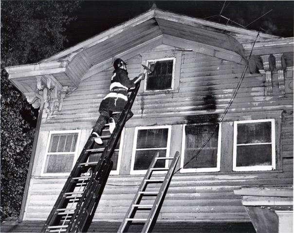 Firefighter at Top of Ladder Using Axe on House Window